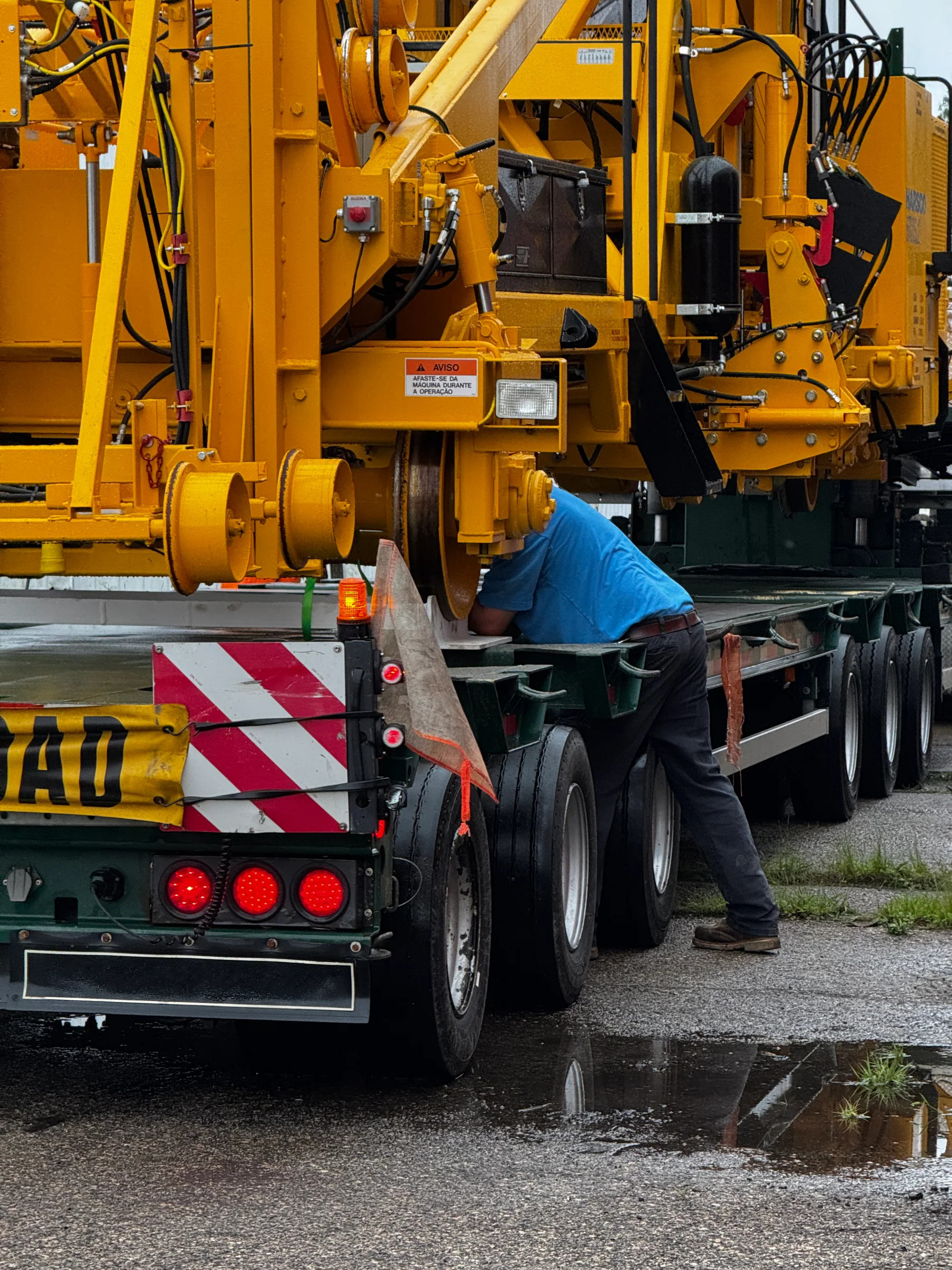 Worker beside the rail wheels of yellow railway equipment positioned on a road trailer.