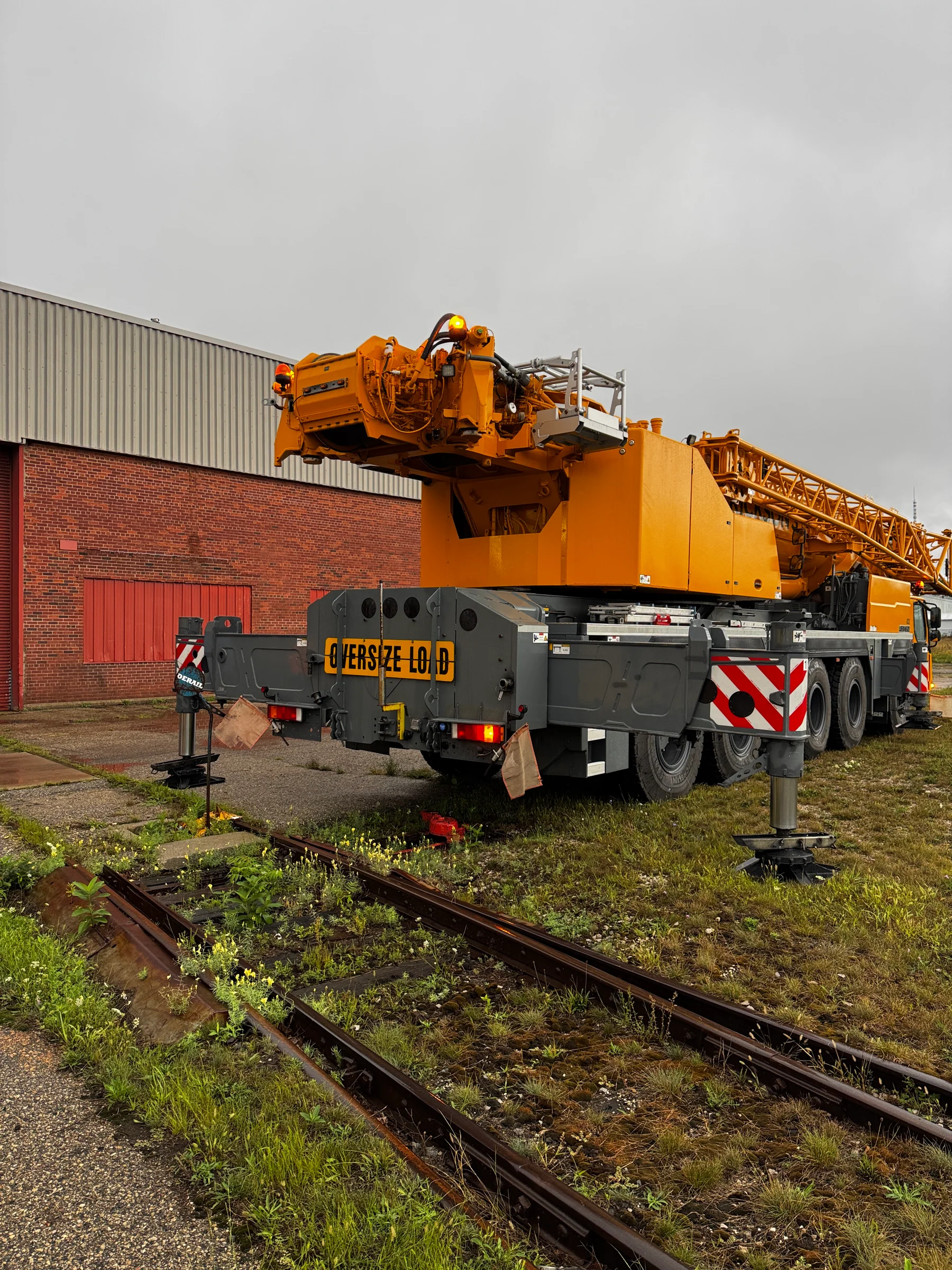 Mobile crane with stabilizers extended next to railway tracks.