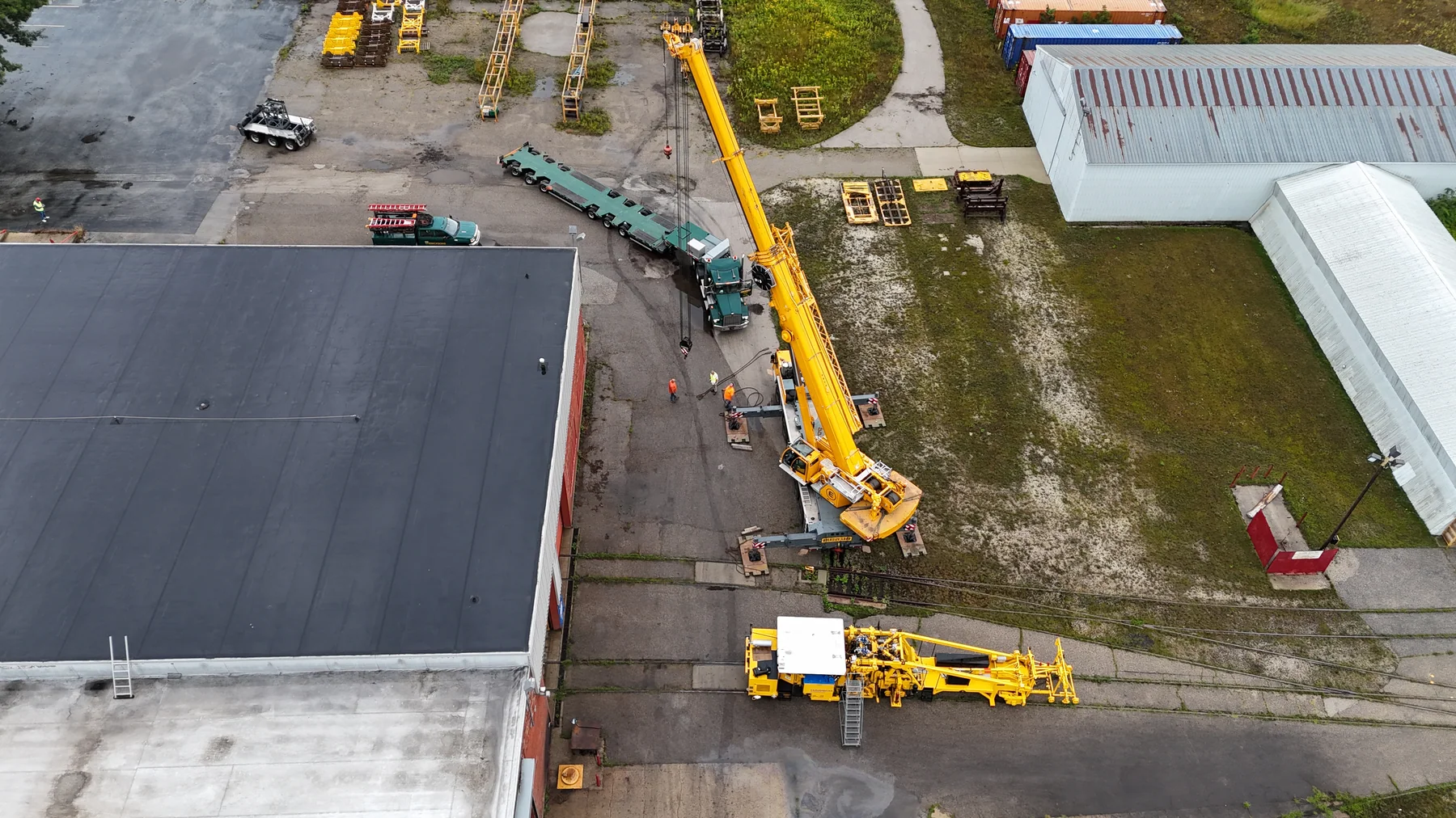 Aerial view of railway equipment, a mobile crane and a long trailer at an industrial site.