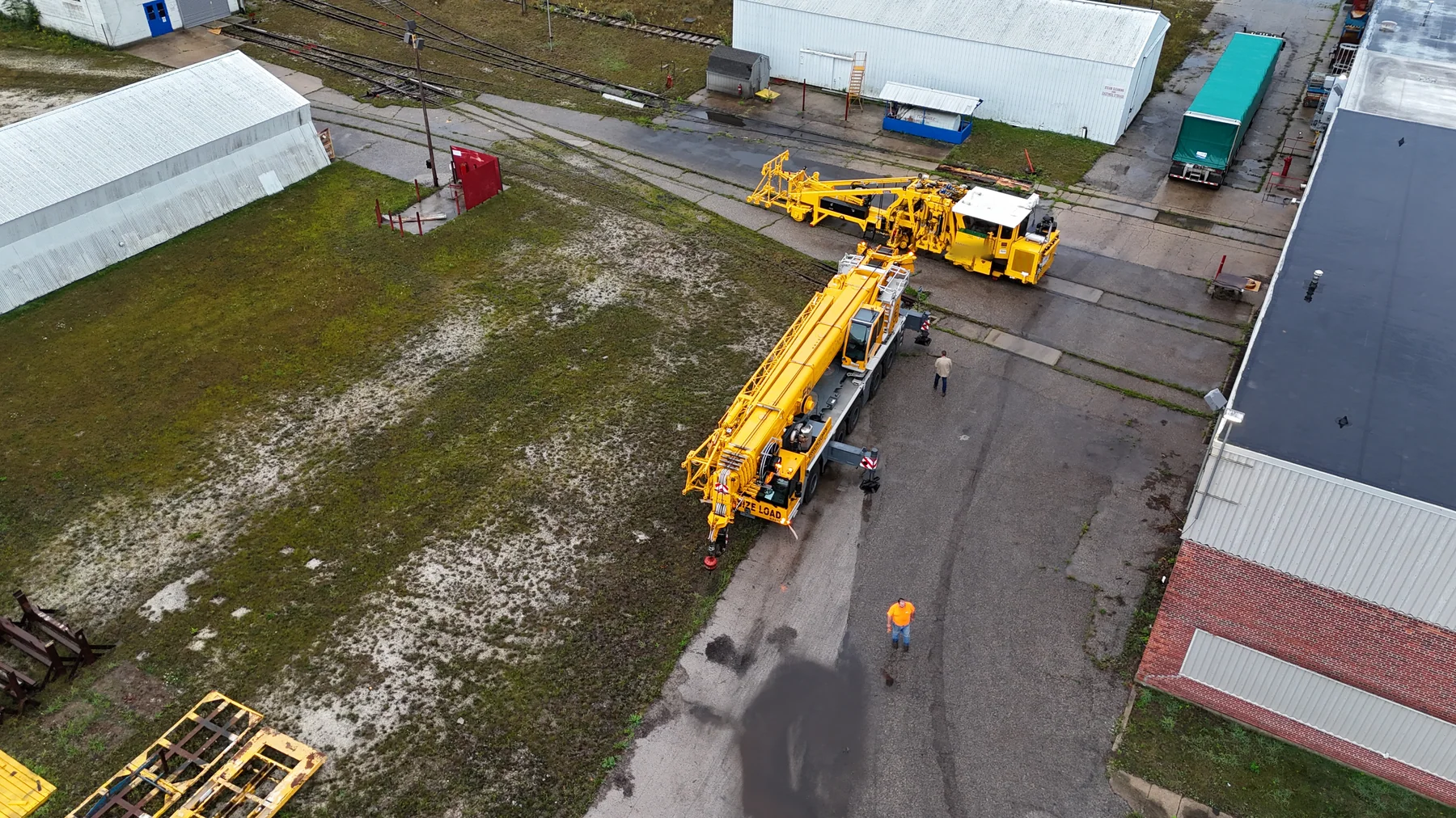 Aerial view of a mobile crane beside yellow railway equipment and rail tracks.