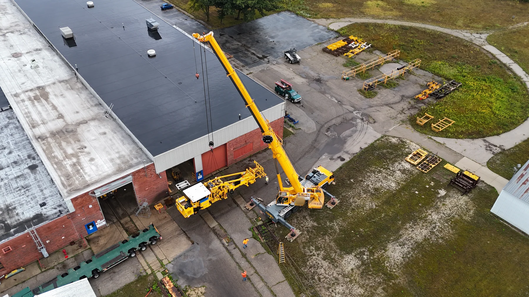 Aerial view of crane cables above yellow railway equipment near an empty long trailer.