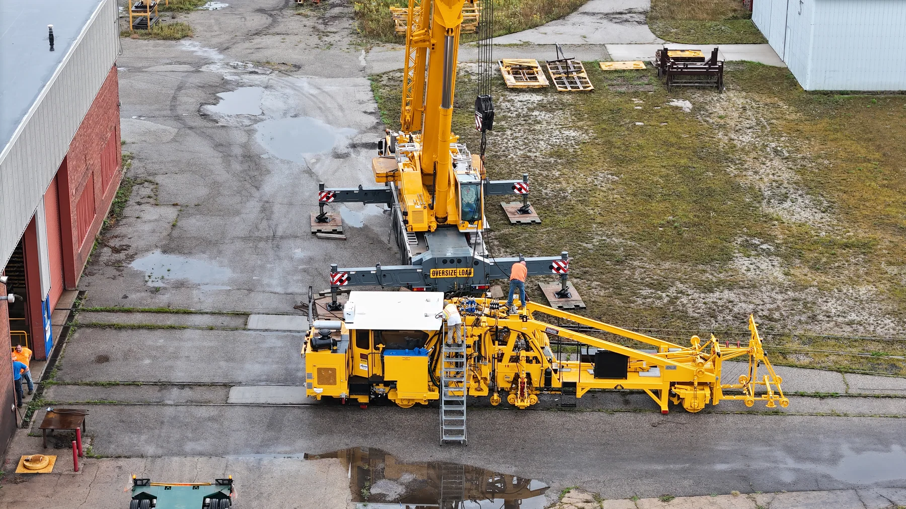 Aerial view of workers beside yellow railway equipment and a mobile crane.